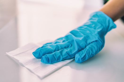 Surface disinfecting home cleaning with sanitizing antibacterial wipes protection against COVID-19 spreading wearing medical blue gloves. Sanitize surfaces prevention in hospitals and public spaces.