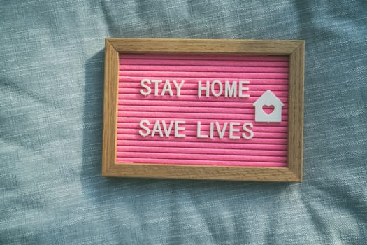Coronavirus quote stay home, save lives pink felt board sign with message of self isolation for social responsability on home sofa background. COVID-19 text to promote staying at home.