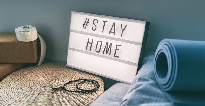 Coronavirus Yoga at home sign lightbox with text hashtag Hashtag STAYHOME glowing in light with exercise mat, cork blocks, strap meditation pillows. COVID-19 banner to promote self isolation staying at home.