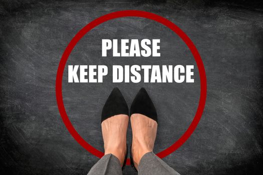COVID-19 Coronavirus health safety message asking shoppers in supermarket to keep distance apart each customer. Top view of feet standing in red circle with text social distancing. Blackboard texture.
