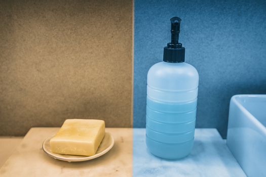 Soap bar versus liquid hand soap bottle comparison of hand washing products on home bathroom vanity. Yellow and blue color boxes to compare.