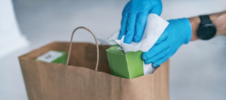 Coronavirus wiping down grocery packages after receiving home delivery wearing gloves, using disinfecting sanitizing wipes to wipe the surfaces clean. Cleaning of COVID-19 virus.