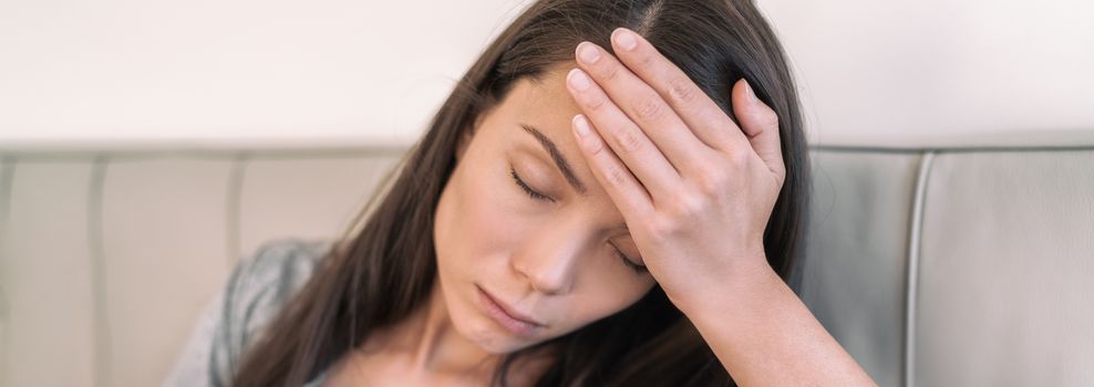 COVID-19 fever Asian woman touching forehead fainting panoramic banner. Coronavirus symptoms include, fever, cough, shortness of breath, in more severe cases, pneumonia.