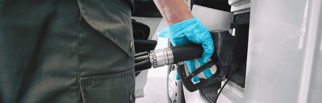 Gas pump Coronavirus outbreak protection gloves for touching handle while pumping gasoline at gas station banner panoramic. Low prices of crude oil plunging during COVID-19 pandemic.