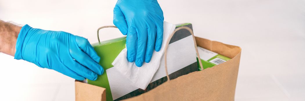 Coronavirus wiping down grocery packages after receiving home delivery wearing gloves, using disinfecting sanitizing wipes to wipe the surfaces clean. Cleaning of COVID-19 virus.