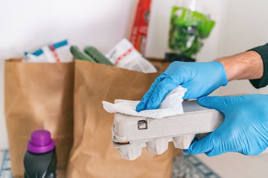 Cleaning groceries man at home wiping egg package with sanitizing wipes at home after shopping or receiving online delivery grocery store bags.