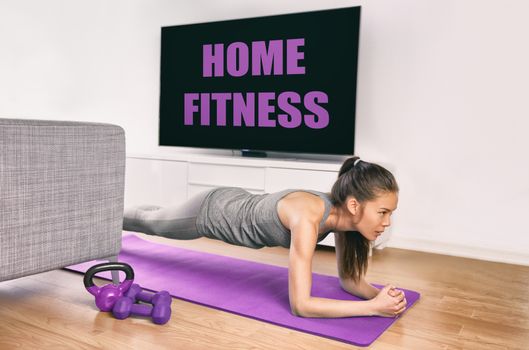 Fitness workout staying at home indoors. Asian girl doing plank exercises to exercise core watching tv videos of fit class. Young woman training muscles in front of the TV without going to the gym.