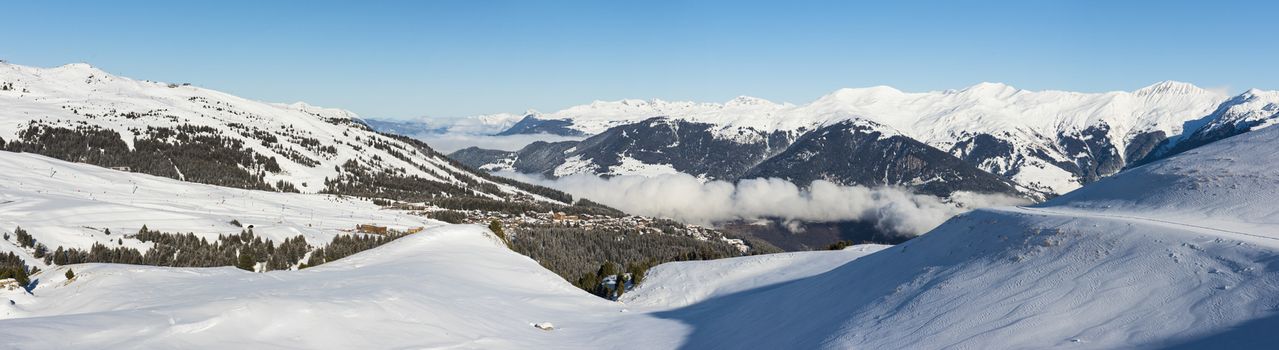 Panoramic view down snow covered valley in alpine mountain range with conifer pine trees and clouds