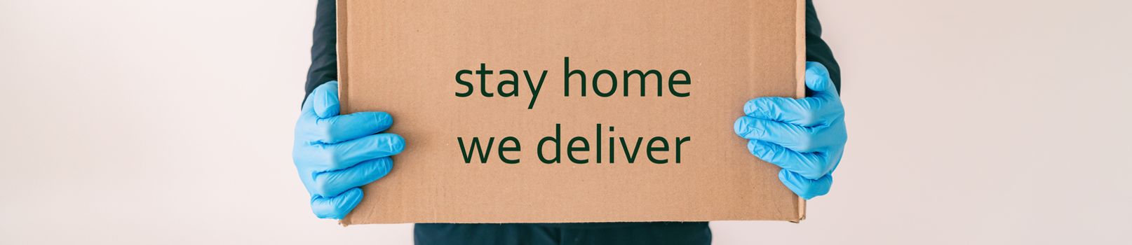 Home delivery with quote STAY HOME WE DELIVER on cardboard box banner. Food grocery delivered with gloves for COVID-19 quarantine from coronavirus social distancing. man giving purchase.
