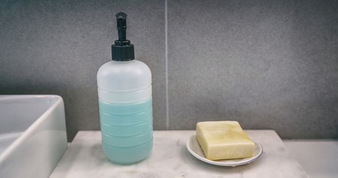 Soap bar versus liquid hand soap bottle comparison of hand washing products on home bathroom vanity counter banner background.