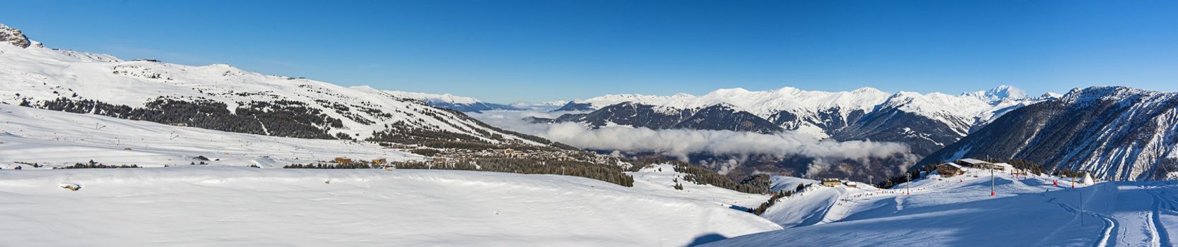 Panoramic view down snow covered valley in alpine mountain range with conifer pine trees and clouds