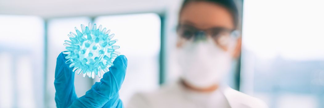 COVID-19 vaccine research worker looking at coronavirus in lab looking for a cure banner panoramic background . Asian woman scientist wearing PPE gloves, mask and goggles.