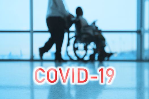 COVID-19 billboard red text on blue medical hospital background with doctor walking with disabled patient in wheelchair.