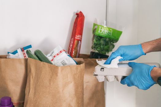 COVID-19: Is it necessary to clean your groceries delivered at home. Man in quarantine wiping cardboard package with sanitizing wipes after shopping or receiving online delivery bags.