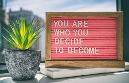 Inspiration quote message sign saying You are who you decide to become - life advice for self esteem, confidence. Home background.