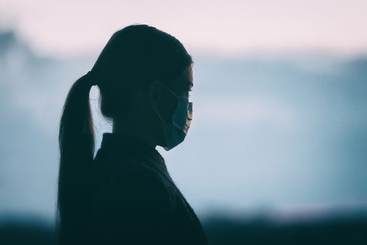 Coronavirus COVID-19 anxiety mental health problem sad woman wearing protective medical face mask silhouette alone thinking of the depressive future of society.