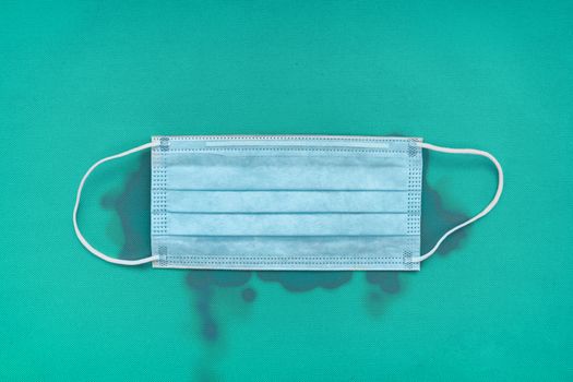 Dirty medical surgical face mask on blue background with design stains dripping concept for COVID-19 coronavirus prevention.