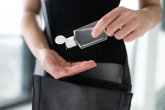 COVID-19 hand sanitizer woman using small portable sanitiser bottle on the go when going out, commuting to work in public space cleaning hands disinfecting with alcohol gel dispenser.