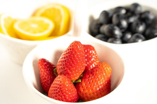 A serving dish filled with strawberries, lemon slices and black grapes against a plain white background