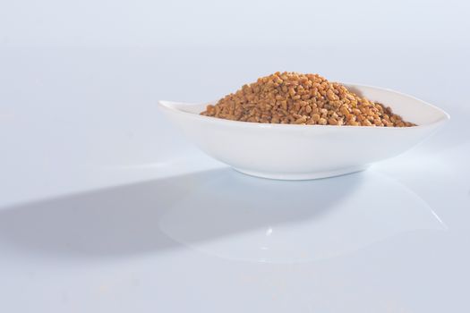 Fenugreek seeds in a white bowl on white background