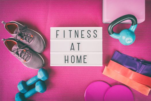 Fitness at home sign with pink yoga mat, running shoes, kettlebell weight and dumbells resistance bands and sliders for pilates online class. Exercise indoors for women.