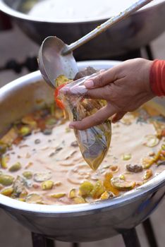 Woman hand holding dipper scooping green curry with chicken Put in a plastic bag And there was a basin with curry on a blurred background.
