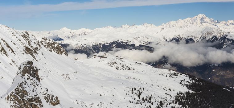 Aerial high angle panoramic view down snow covered valley in alpine mountain range with cumulus clouds