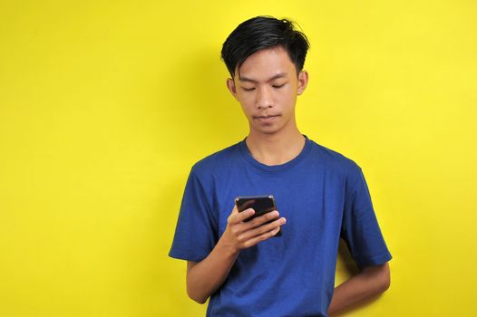 Portrait of serious Asian man using smartphone isolated on yellow background