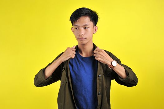 Portrait of young Asian man doing arrogant gesture, isolated on yellow background