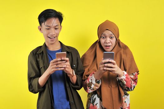Woman and Young man, shock looking at smartphone display with positive emotion facial expression isolated yellow background