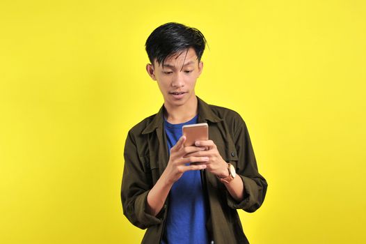 Shocked face of Asian man in white shirt looking at phone screen, isolated on yellow background.