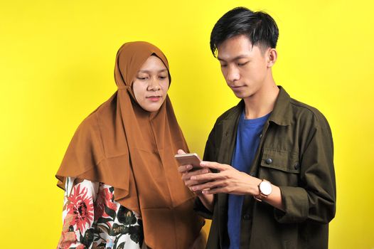 Portrait of two people look at smartphone display, isolated on yellow background