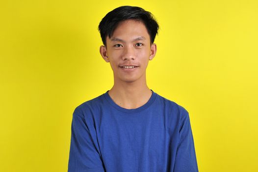 Portrait of happy young Asian man smiling in front of the camera, isolated on yellow