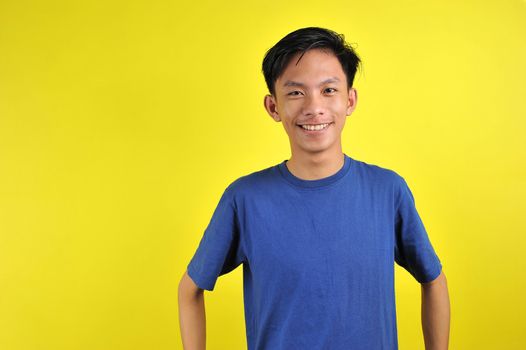 Portrait of happy young Asian man smiling in front of the camera, isolated on yellow