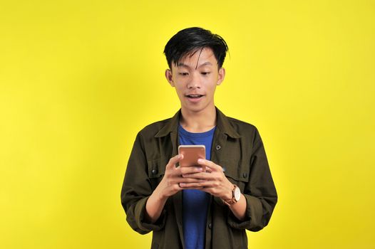 Shocked face of Asian man in white shirt looking at phone screen on yellow background.
