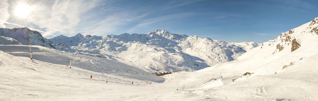 View down a snowy piste with skiers and mountain valley