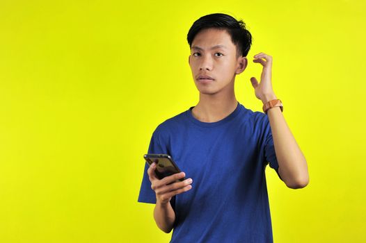 Portrait of confused man looking at smartphone, isolated on yellow background