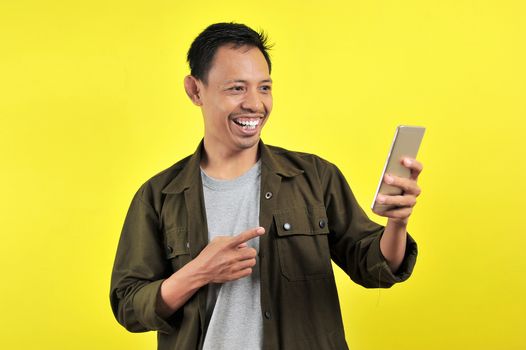 Happy of young good looking Asian man smiling using smartphone isolated on yellow background