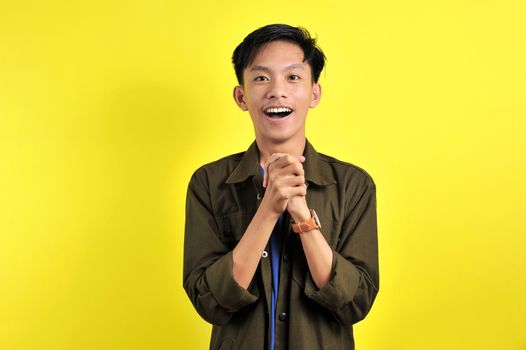 Portrait of happy Young Asian man surprised and shocked, isolated on yellow