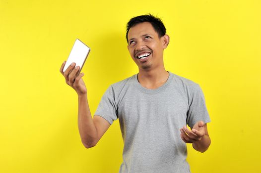 Funny Young Asian man holding smartphone, isolated on yellow background