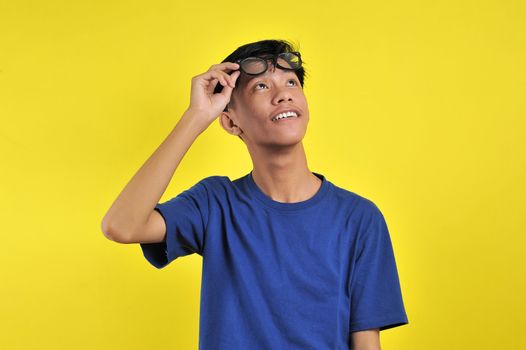 Happy Young Asian man smiling wearing glasses look at copy space, isolated on yellow background