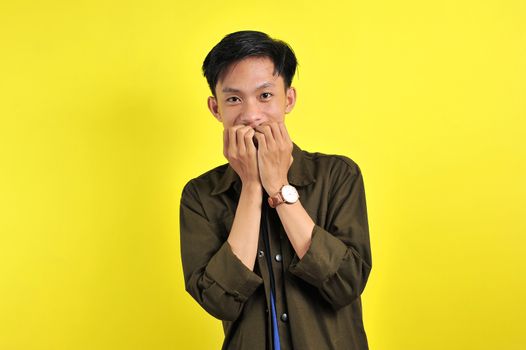 Handsome young man looking afraid, stressed and nervous with hands on mouth biting nails, over yellow background