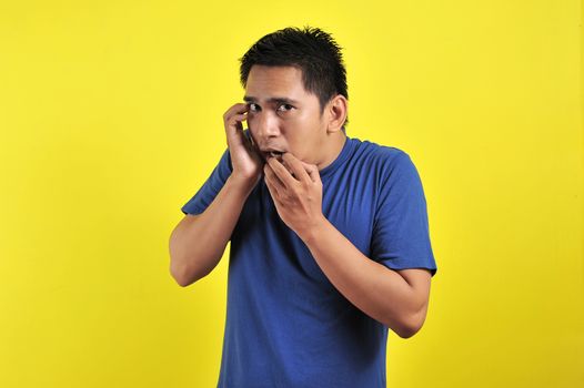 Handsome young man looking afraid, stressed and nervous with hands on mouth biting nails, over yellow background
