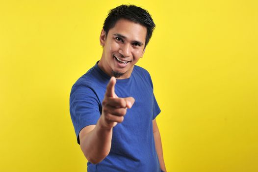 Happy young Asian man smiling pointing to the camera, isolated on yellow