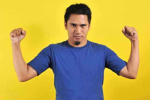 Handsome young Asian man showing muscle, strong gesture and showing power, isolated on orange background