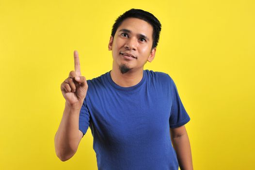 Friendly-looking lively pleasant Asian male with white t-shirt smiling delighted look at copy space joyful. Self-assured pointing, on yellow background