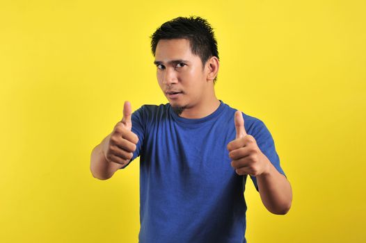 Happy young Asian man giving two thumbs up, isolated on light orange background