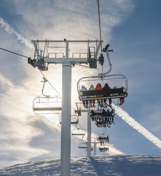 Chairlift with skiers in the sun going over a snowy alpine mountain