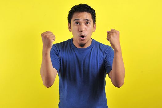 Young asian man happy and excited expressing winning gesture. Successful and celebrating on yellow background
