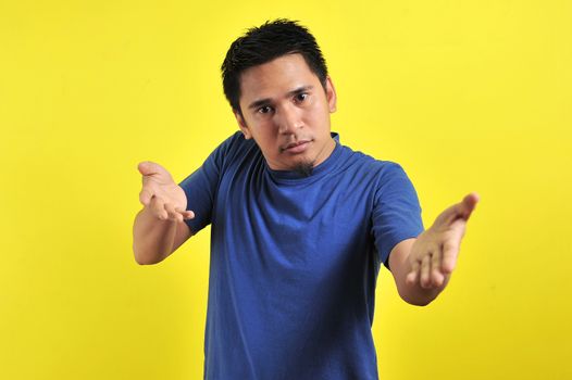 Young man asking questions with hands raised, isolated on yellow background